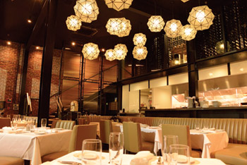 Upscale restaurant open room with white table linens and eclectic lighting above.